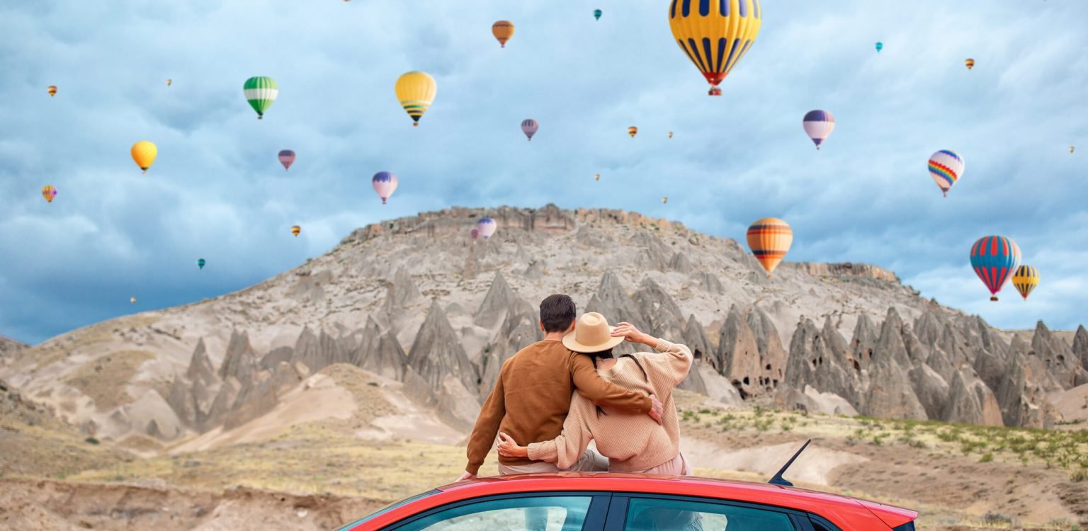 Happy man on summer vacation in famous place. Cave formations. Happy couple on vacation by car in Cappadocia with hot air balloons in the background. Cave formations. Hot air balloon flights.