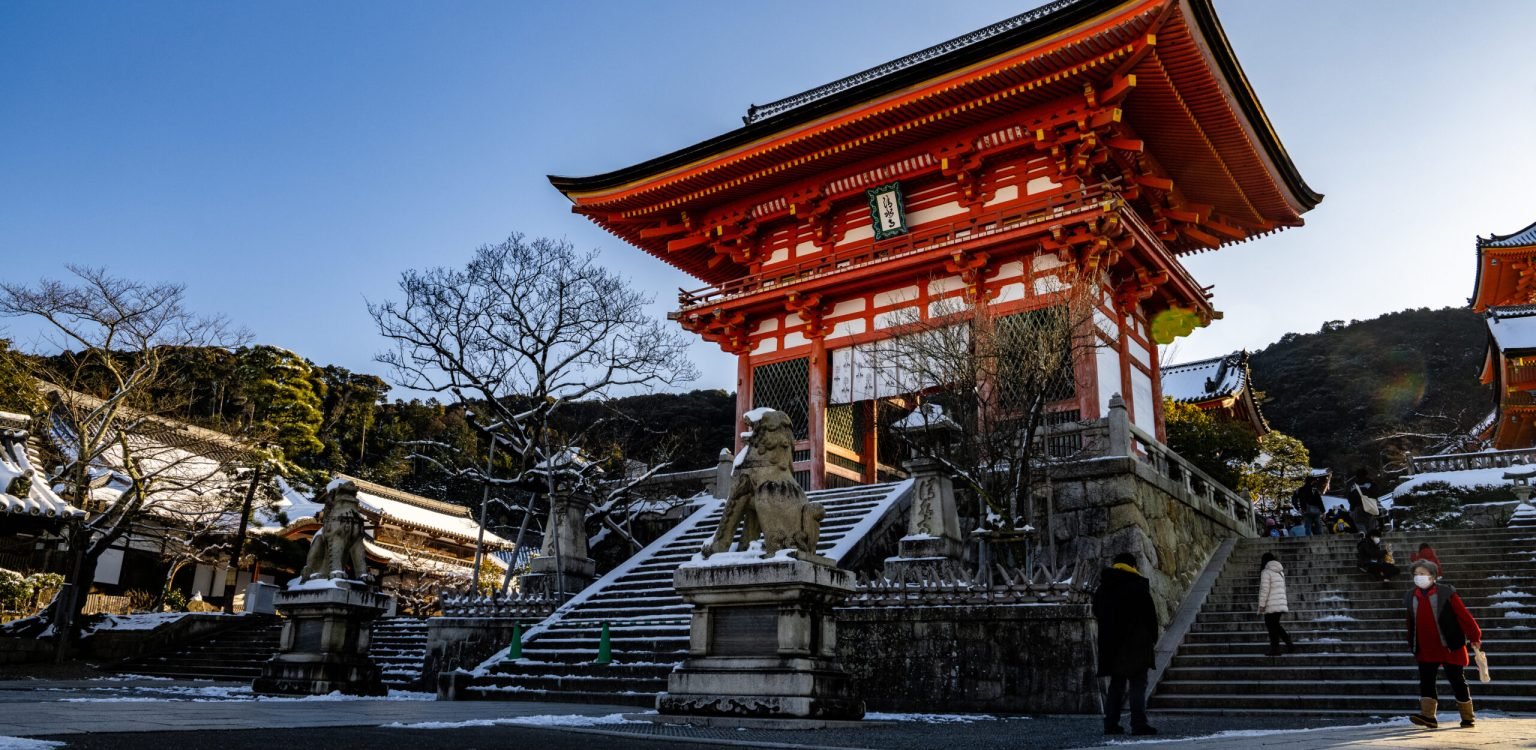 Early morning view of rare snow covered Kiyomizudera Buddhist Temple with ancient bright orange pagodas, statues, gates, and a temple complex in Kyoto